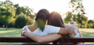 Close up rear view of two women embracing on a park bench.