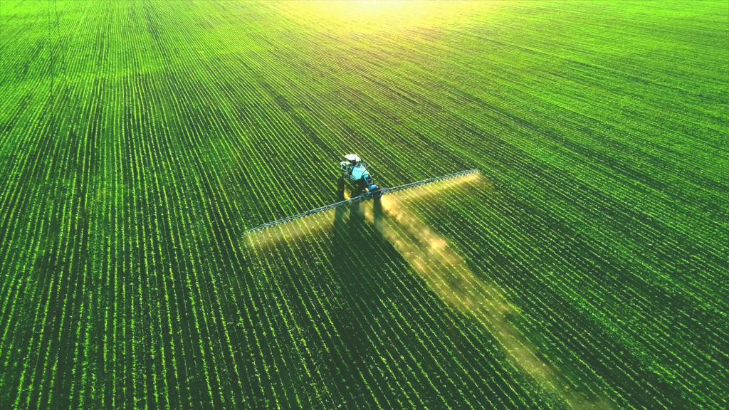 A Tractor spraying fertilizer on green field.